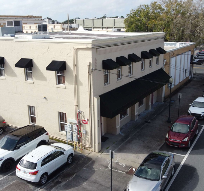 Corner building with black awnings beside a street and parked cars under a clear sky