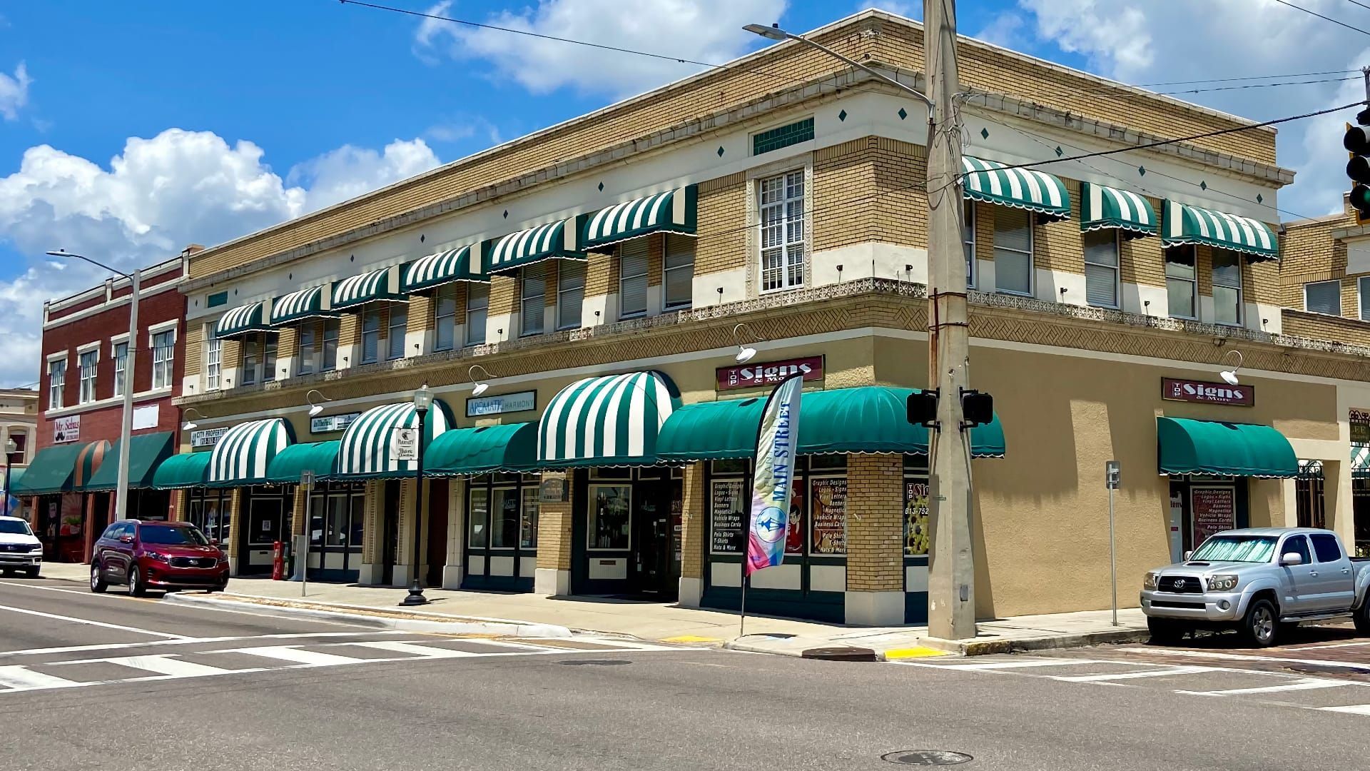 Corner brick storefronts with green-and-white striped awnings on a sunny street corner.