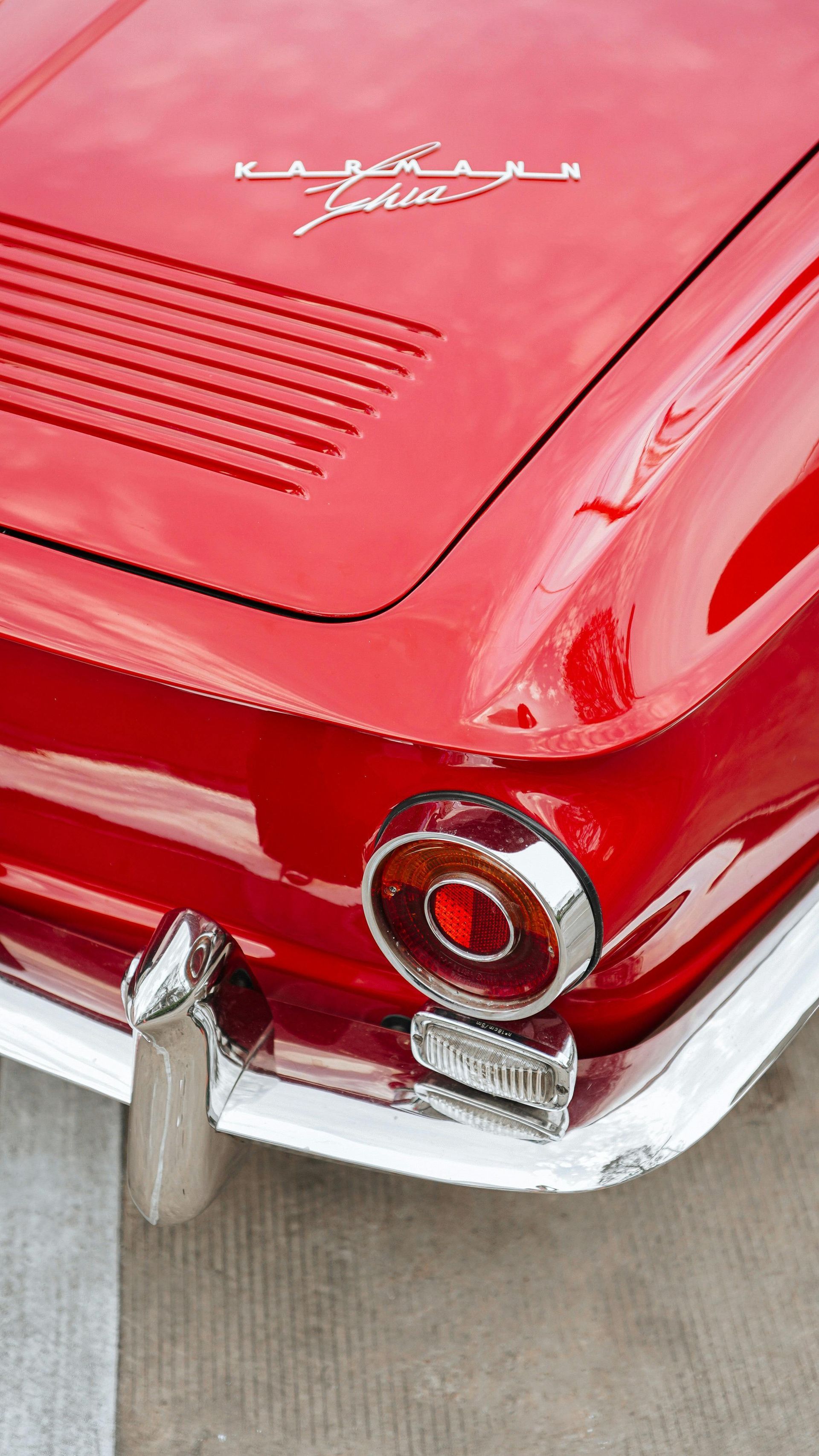 Red vintage Karmann Ghia car rear detail, chrome accents, and taillight.