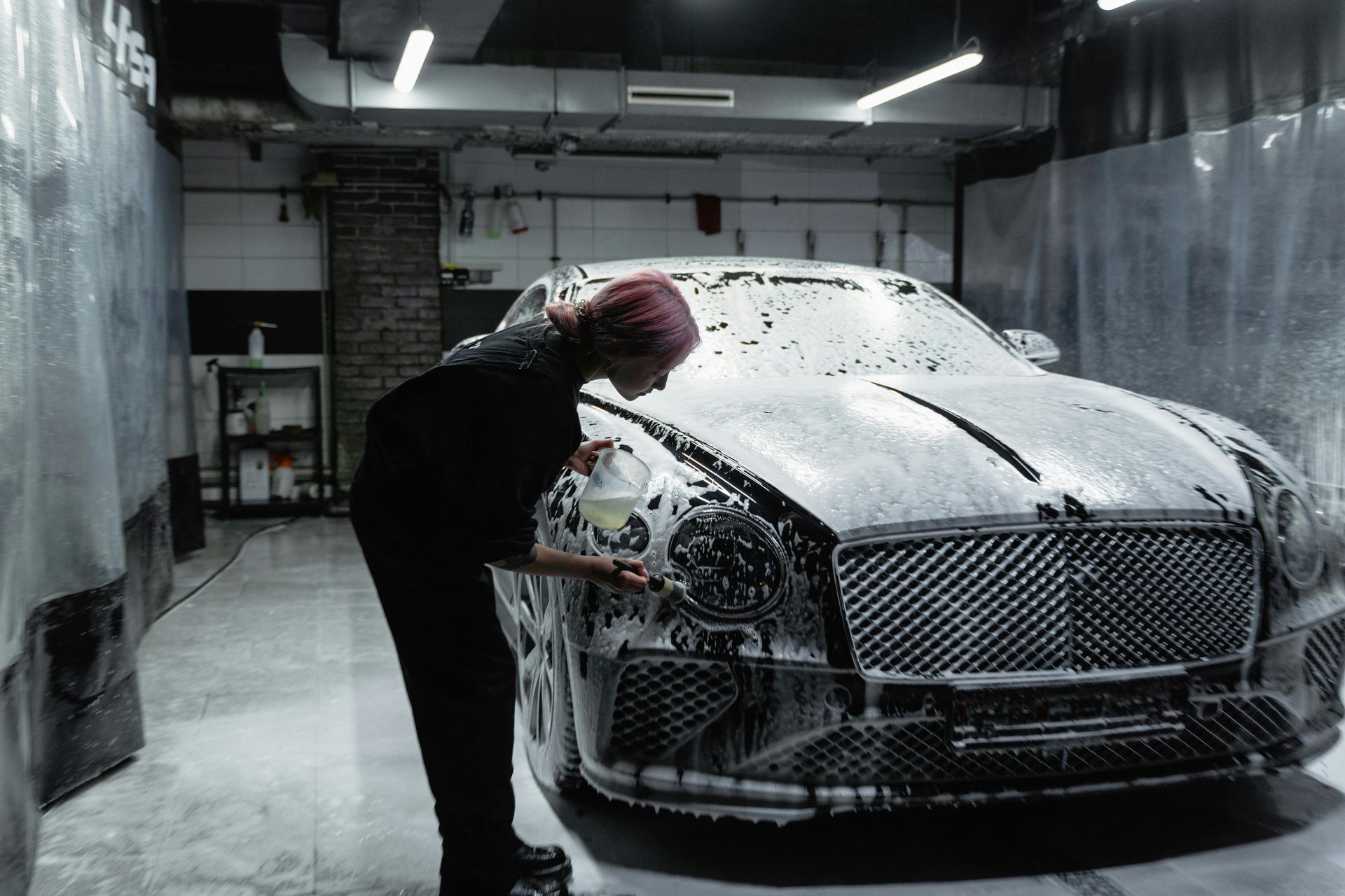 Person washing a Bentley covered in suds in a car wash.