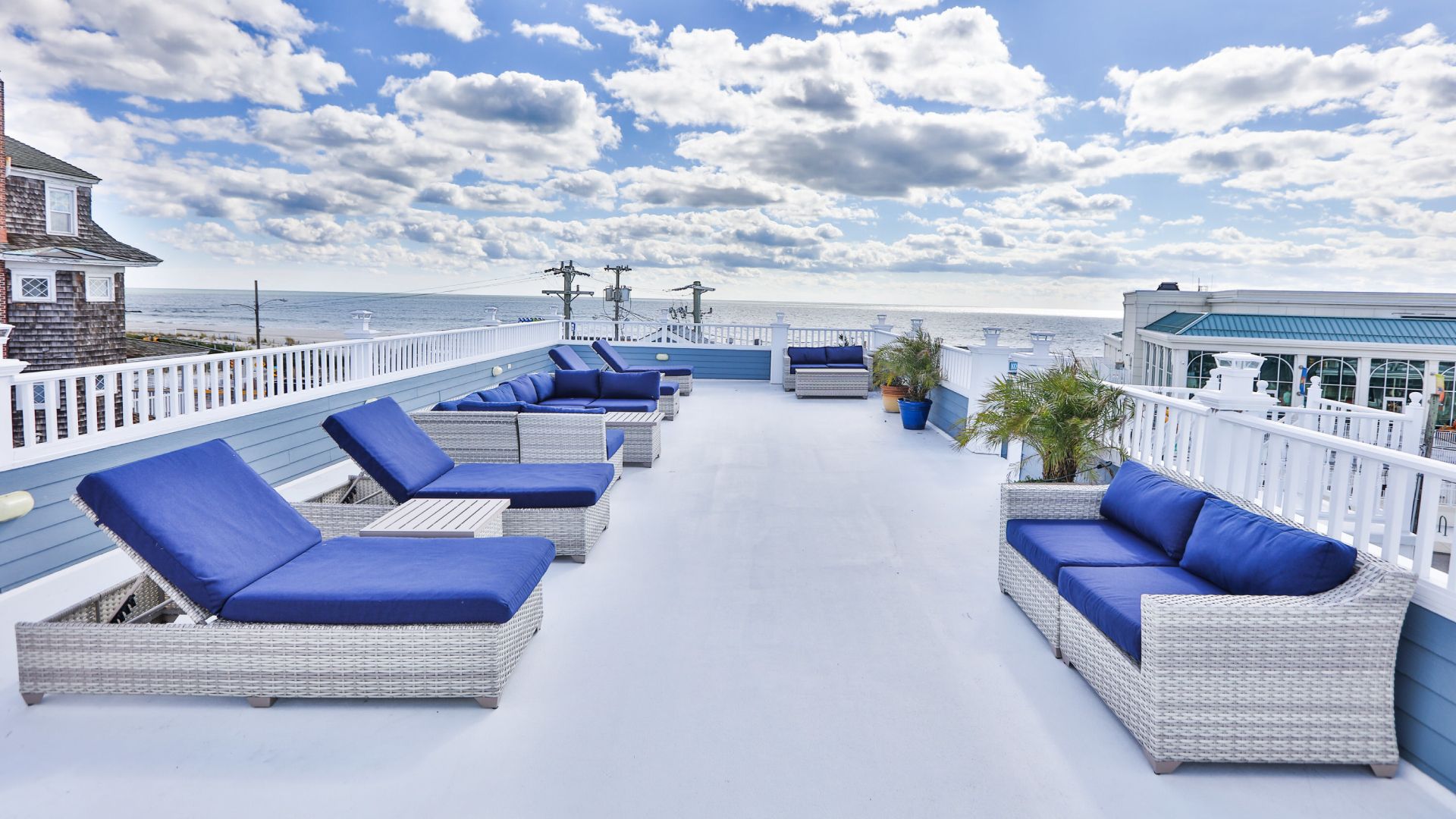 A rooftop deck with blue chairs and a couch overlooking the ocean.