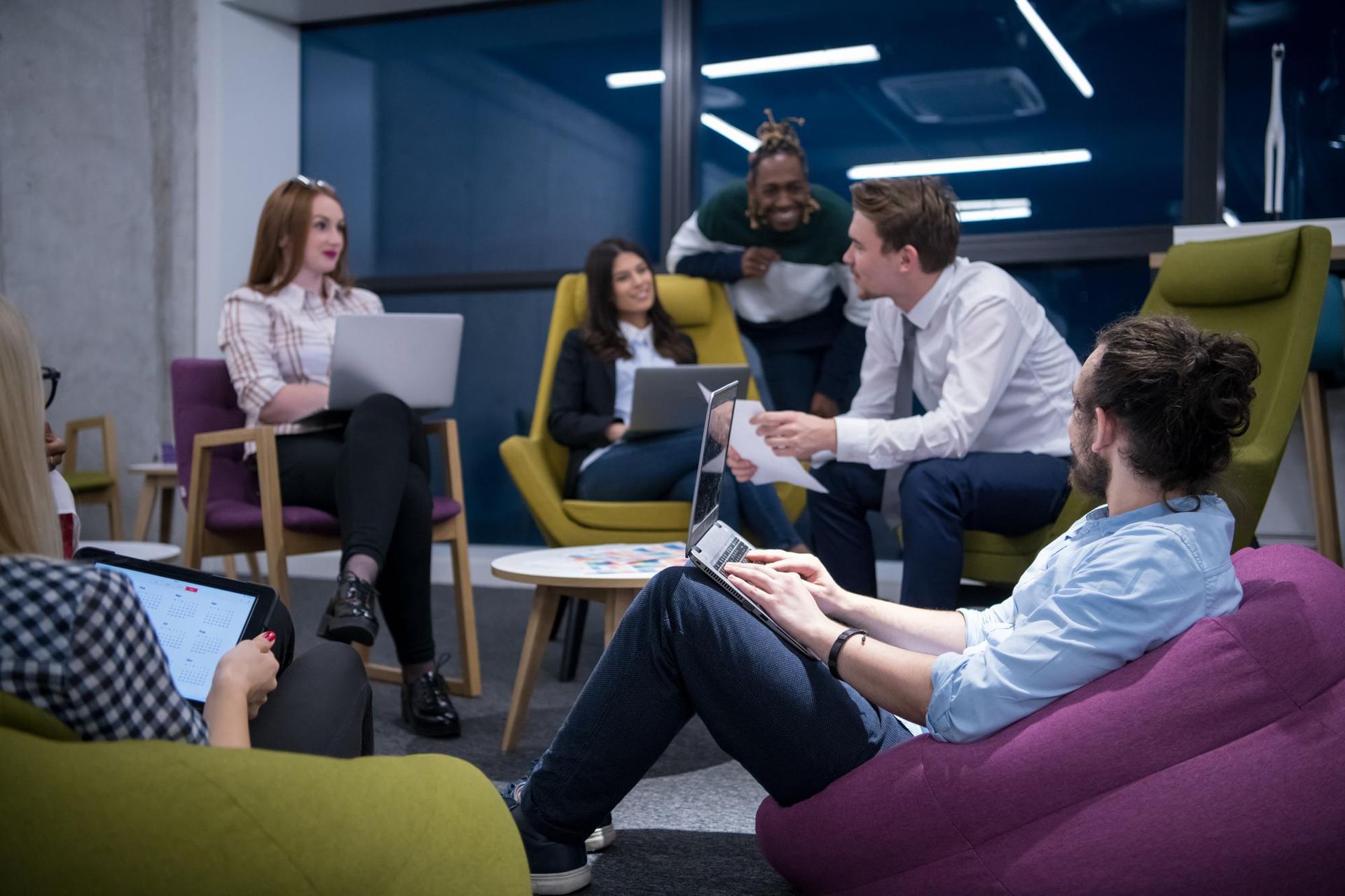 A diverse group of people in a modern office setting collaborating with laptops and papers.