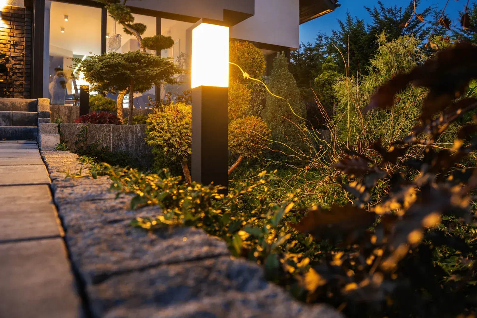 A lamp post in a garden next to a house at night.