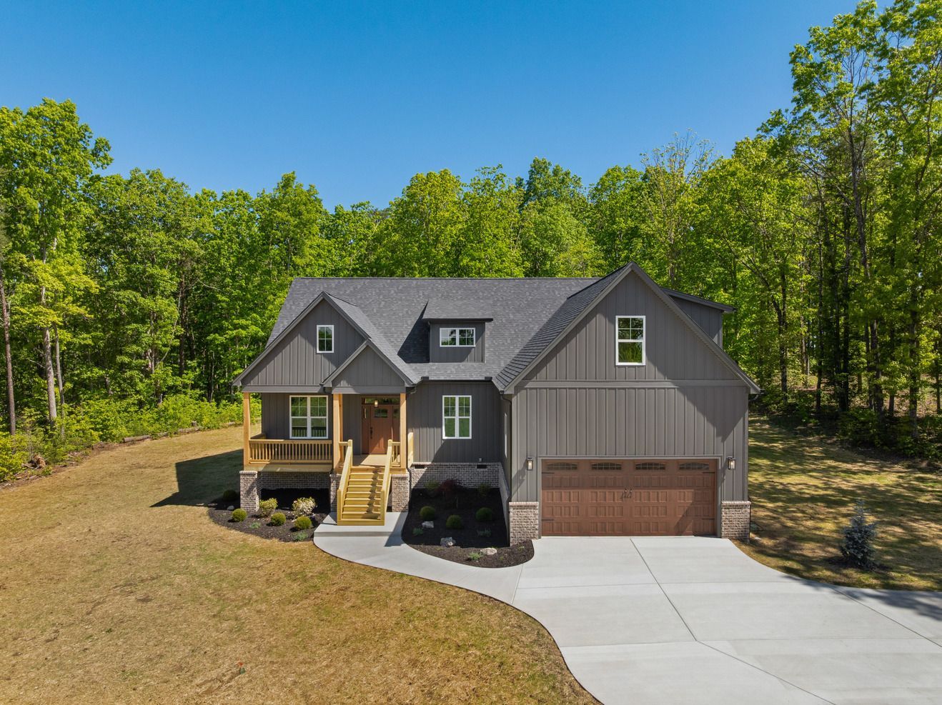 Gray two-story house with attached garage and driveway, surrounded by trees under a blue sky