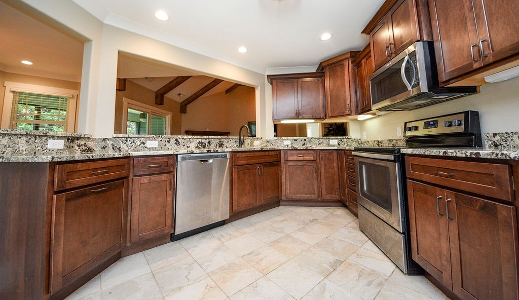 Kitchen with stainless steel appliances, dark wood cabinetry, granite countertops, and tile flooring in open-concept layout.