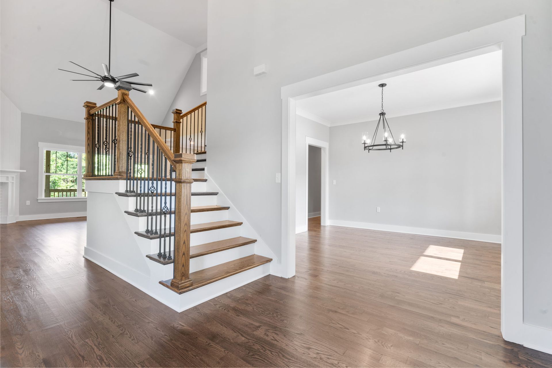 Bright open foyer with curved staircase, hardwood floors, and adjacent dining room with chandelier