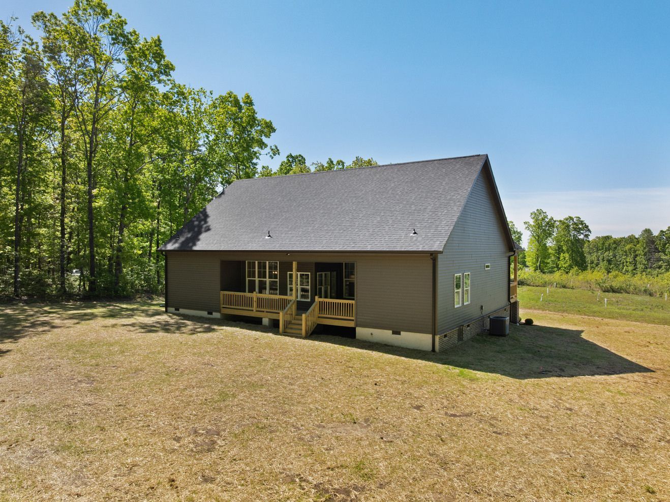 Small gray house with a dark roof and front porch in a sunny grassy yard near trees.