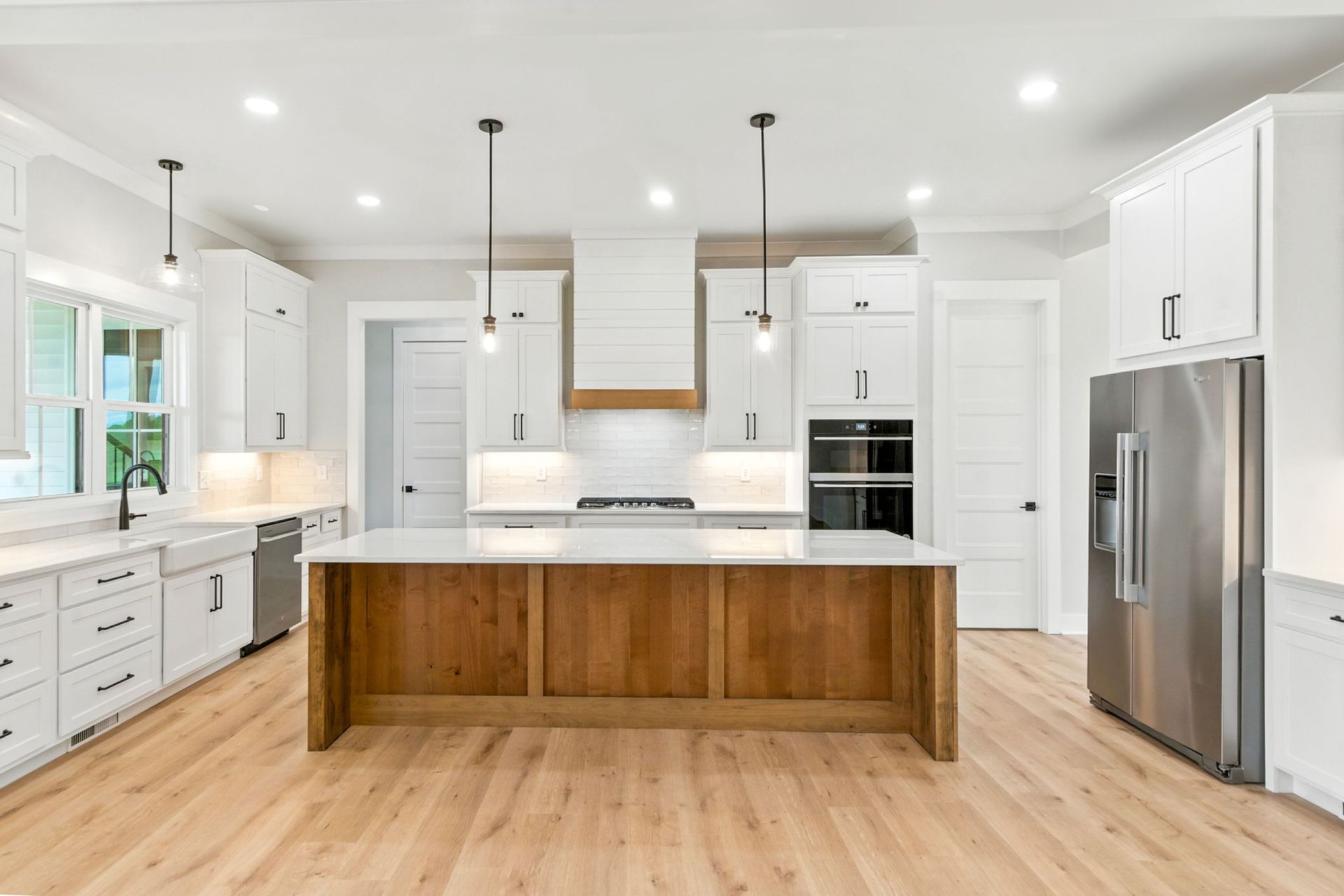 Bright modern white kitchen with wood island, stainless steel fridge, and pendant lights