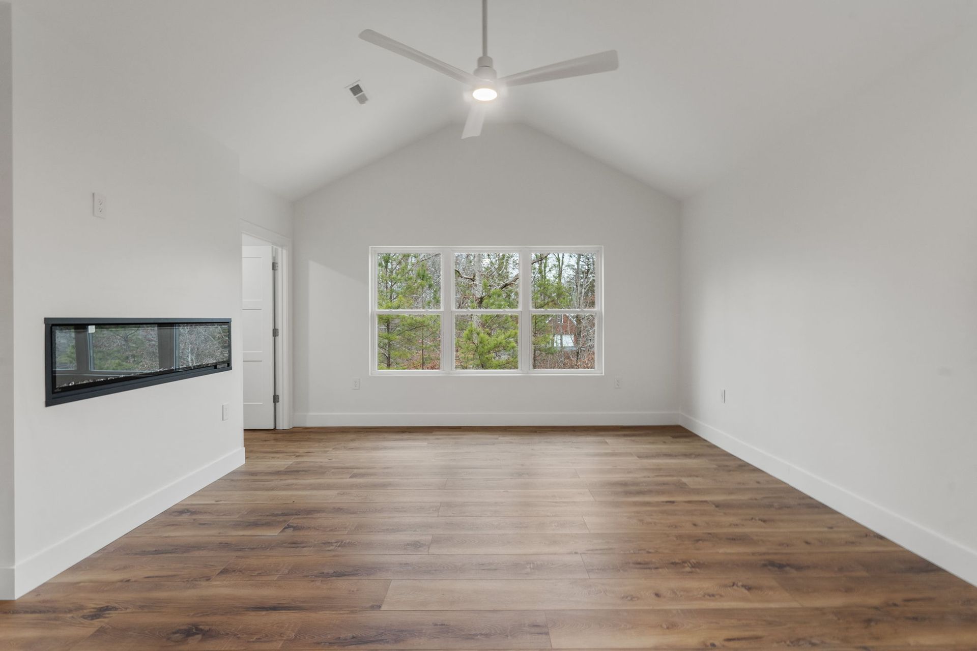 Spacious modern bedroom with vaulted ceiling, large windows, and sleek electric fireplace — designed by custom home builder in Chattanooga.