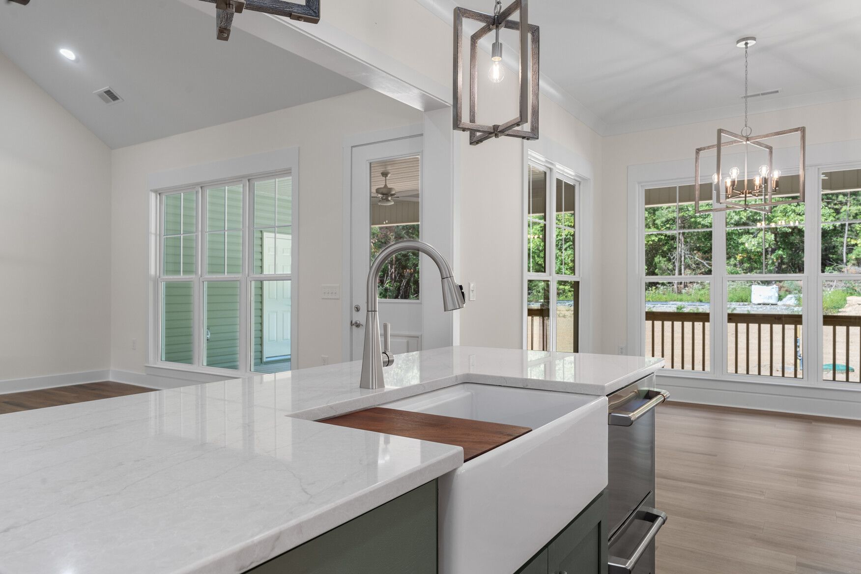 Bright modern kitchen with white island, chrome faucet, and large windows overlooking a deck.