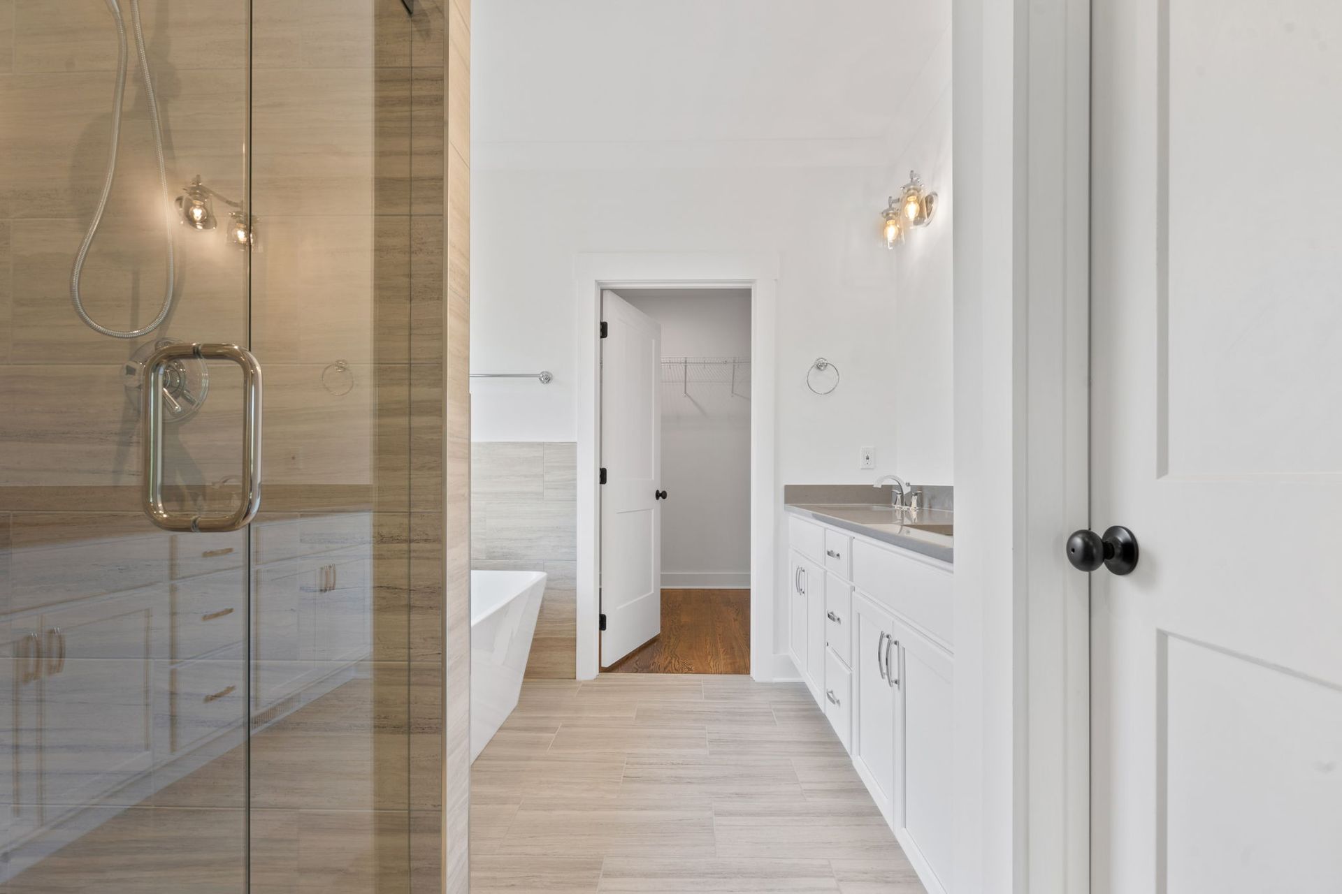 Bright modern bathroom with glass shower, white vanity, and beige tile floor