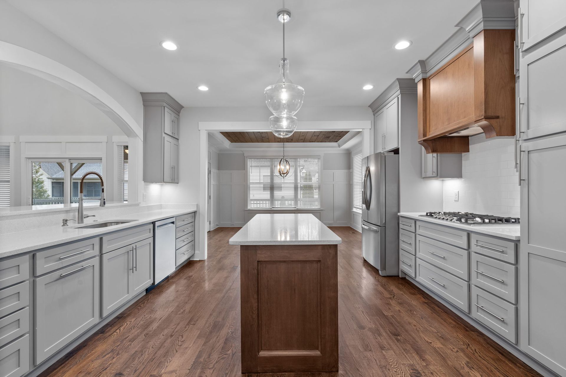 Bright modern kitchen with white cabinets, gray island, stainless appliances, and hardwood floors