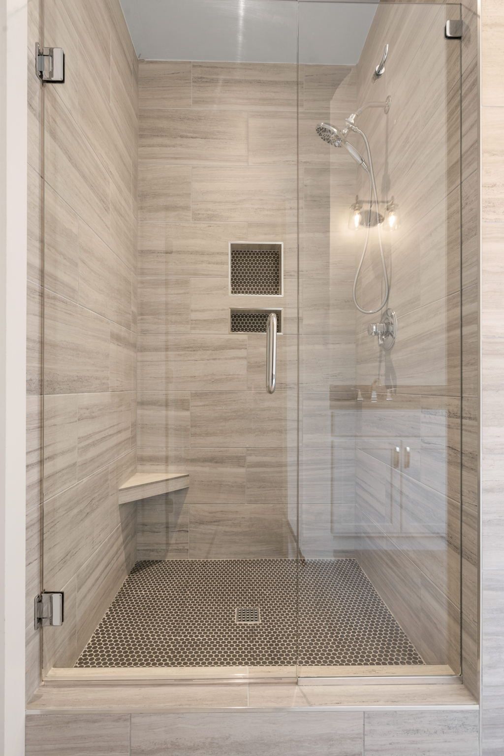 Glass walk-in shower with beige tile walls, mosaic floor, and chrome fixtures