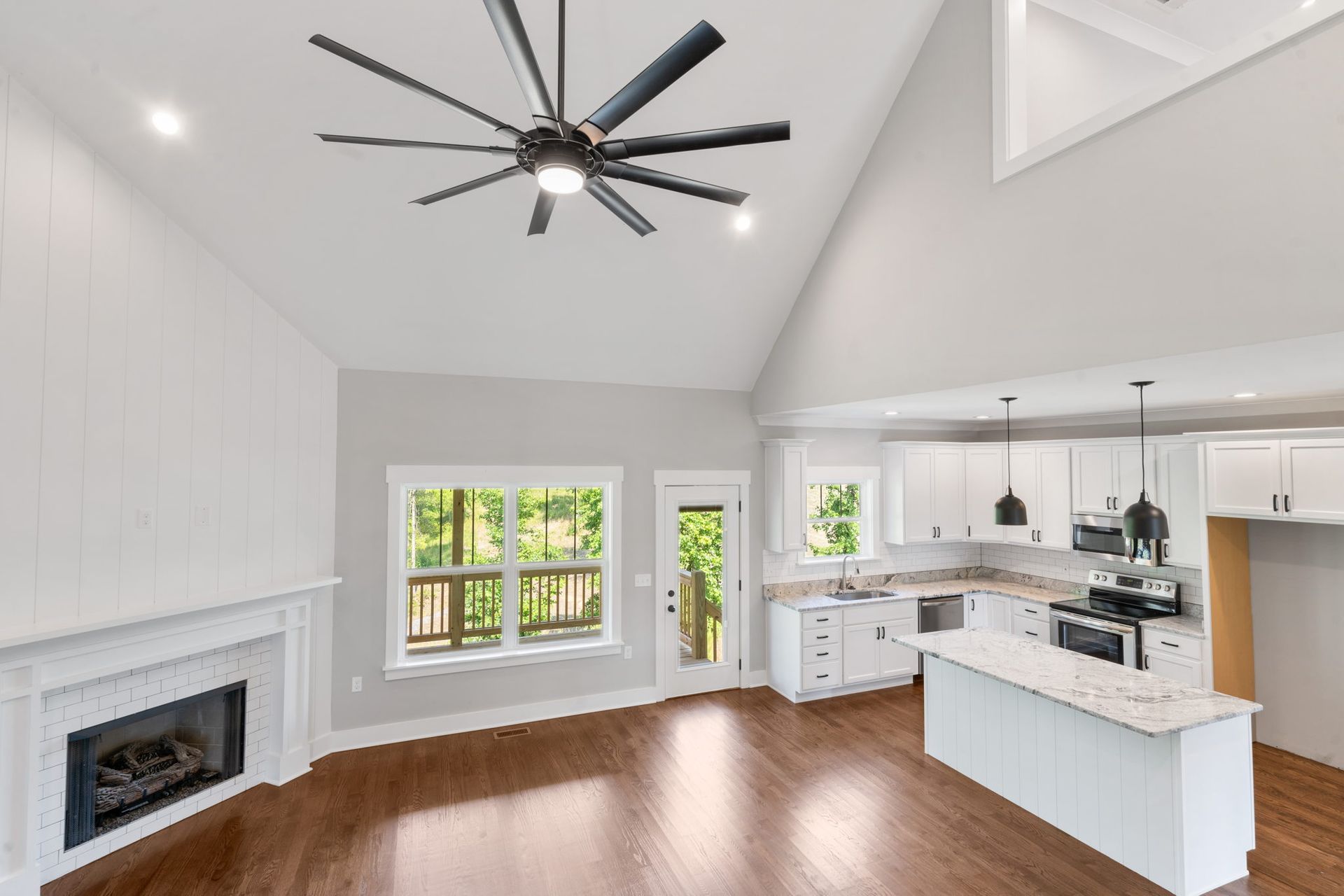 Bright open living room and kitchen with white walls, fireplace, wood floors, and large ceiling fan