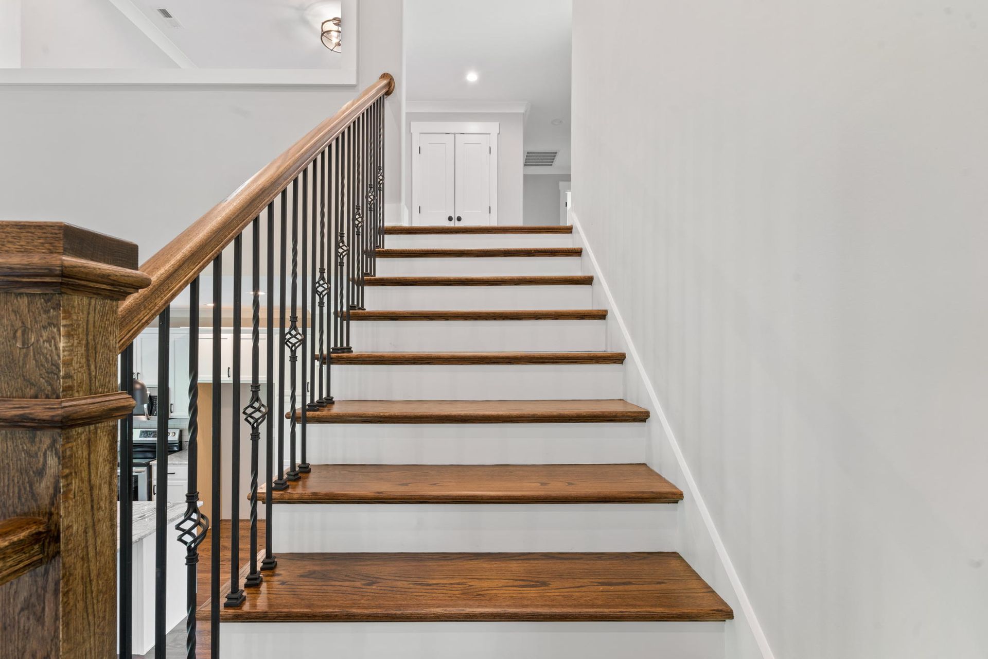 Staircase with wood steps, black railing, and white walls in a bright hallway