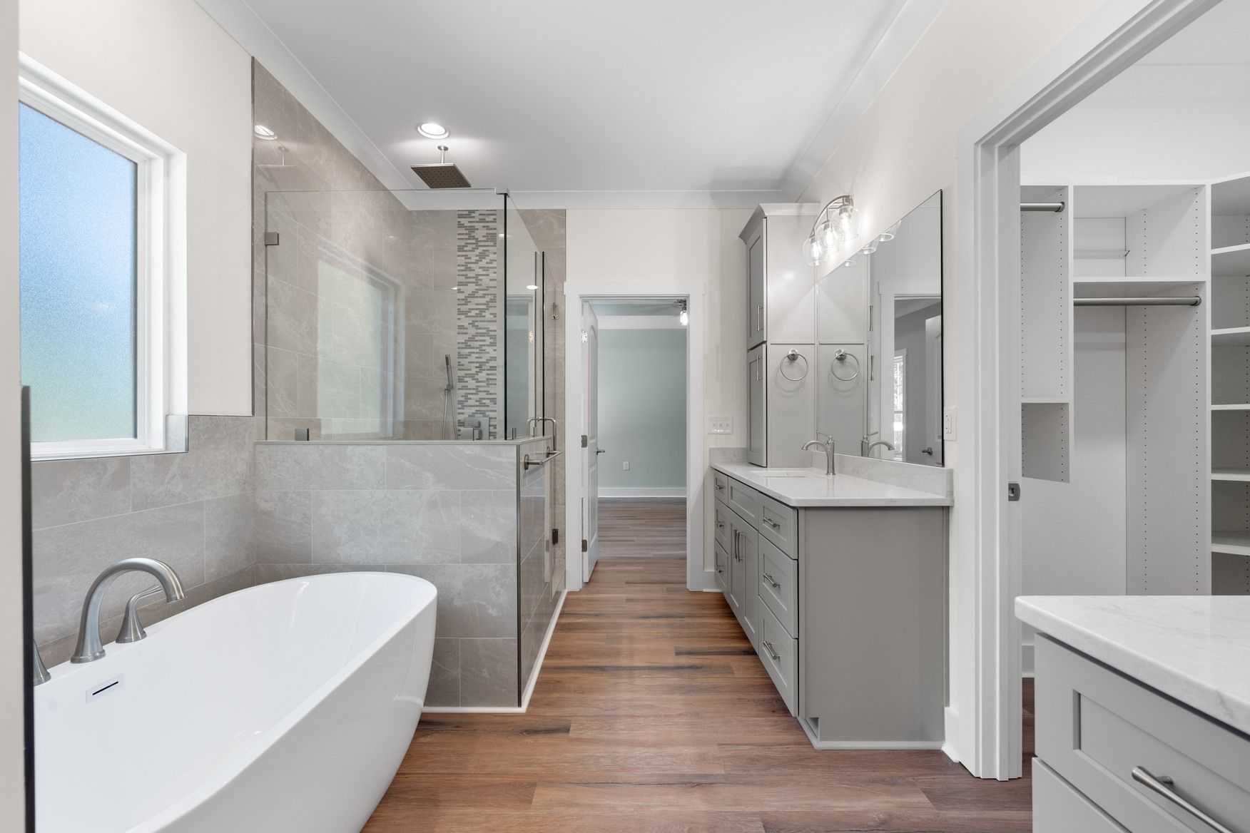 Bright modern bathroom with freestanding tub, glass shower, double vanity, and wood flooring
