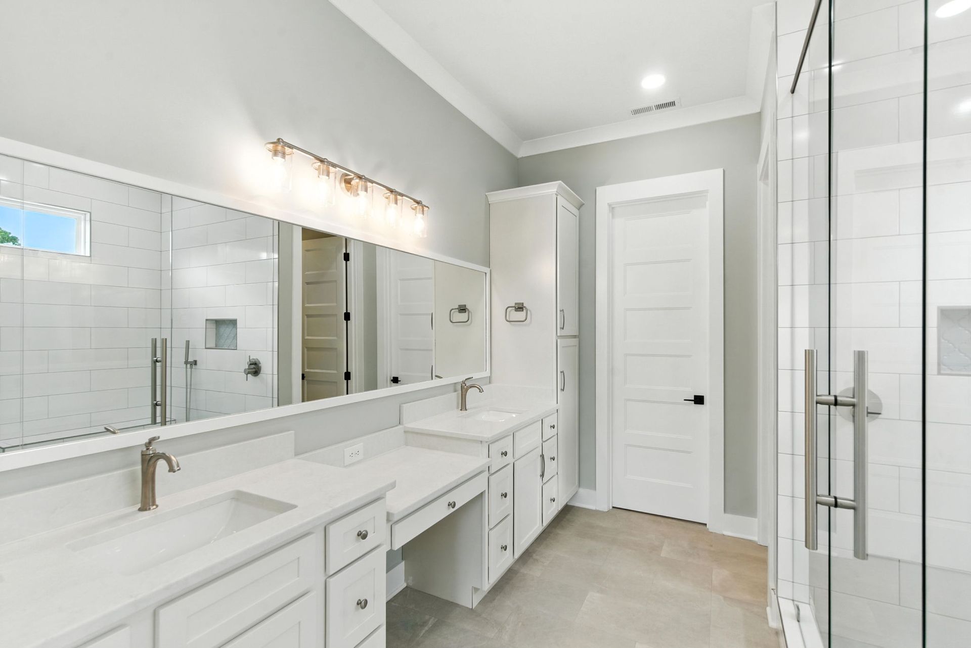 Bright modern bathroom with double vanity, large mirror, white cabinets, and glass shower enclosure