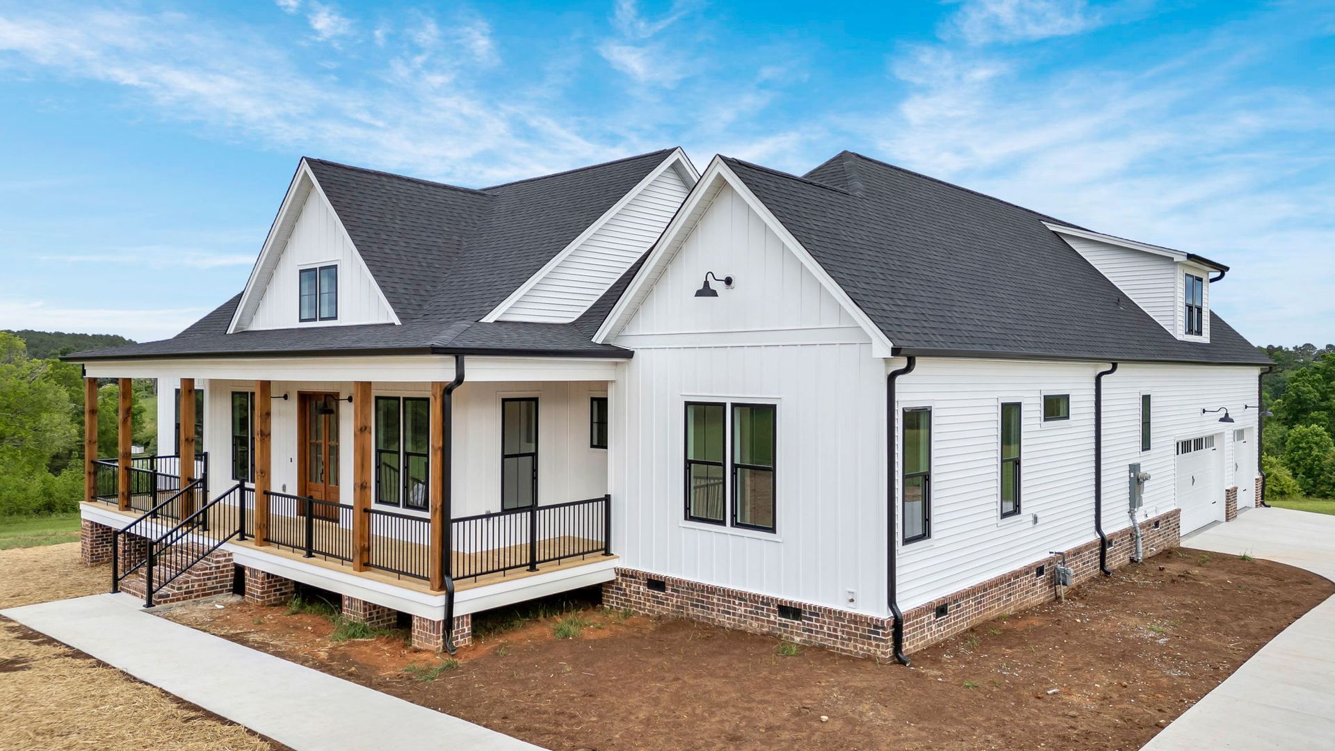 White farmhouse-style house with dark roof and covered porch on a dirt lot under a blue sky