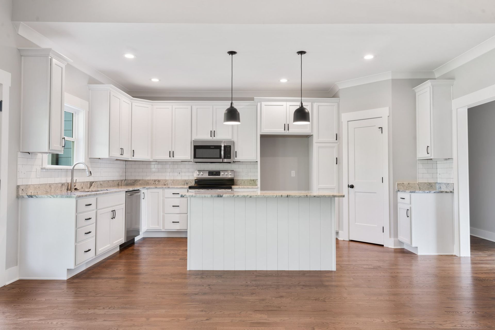 Bright white modern kitchen with island, stainless appliances, and hardwood floors