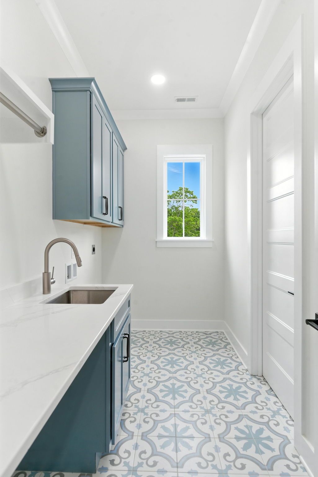 Narrow blue-and-white laundry room with sink, cabinets, and patterned tile floor.