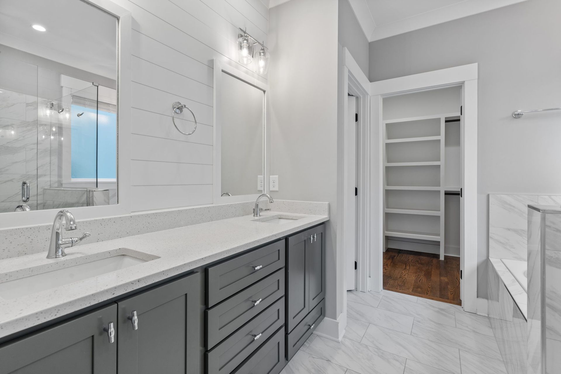 Bright modern bathroom with gray vanity, white countertop, large mirror, and open closet doorway