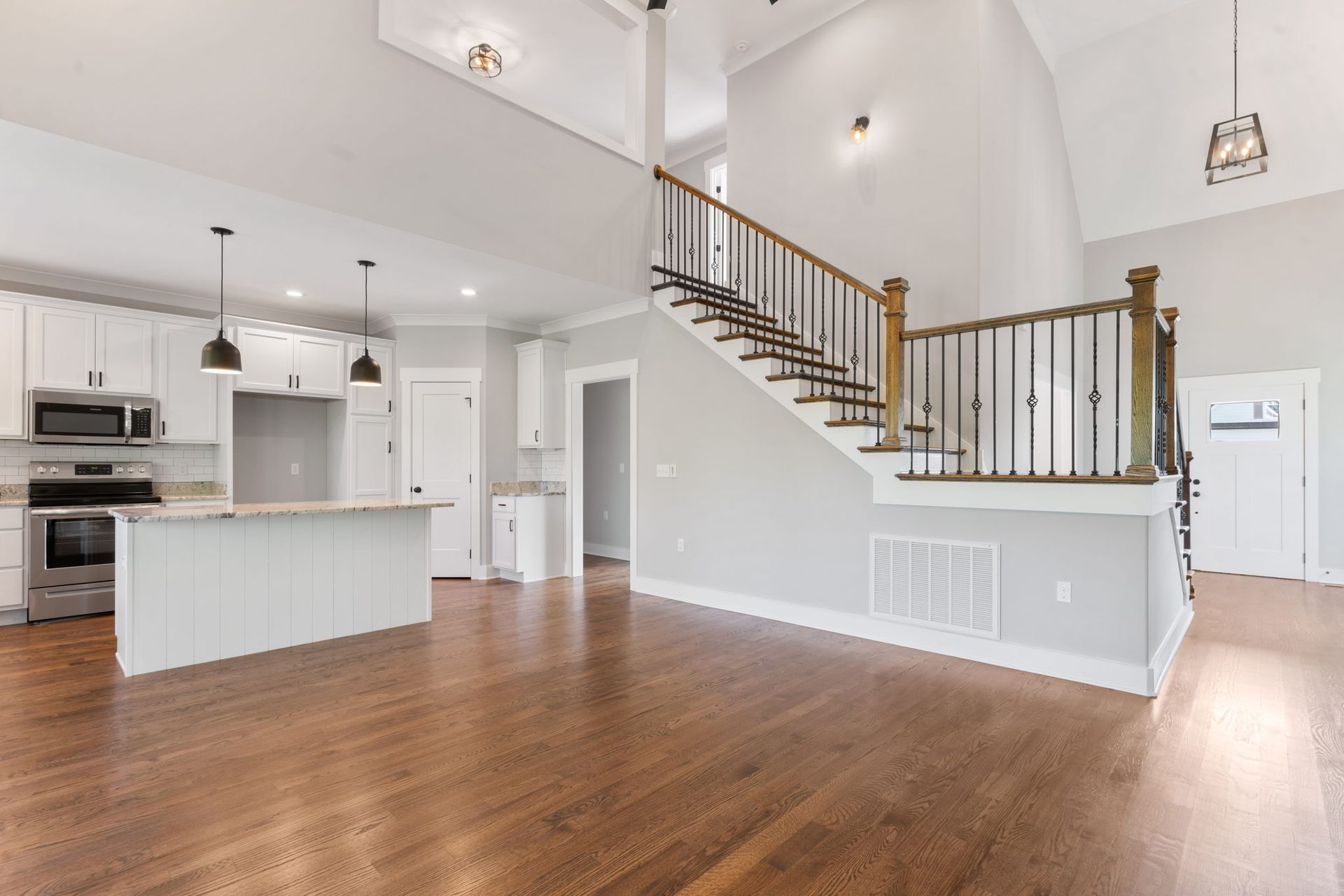 Bright open-plan kitchen and living room with white walls, wood floors, and a staircase to an upper level