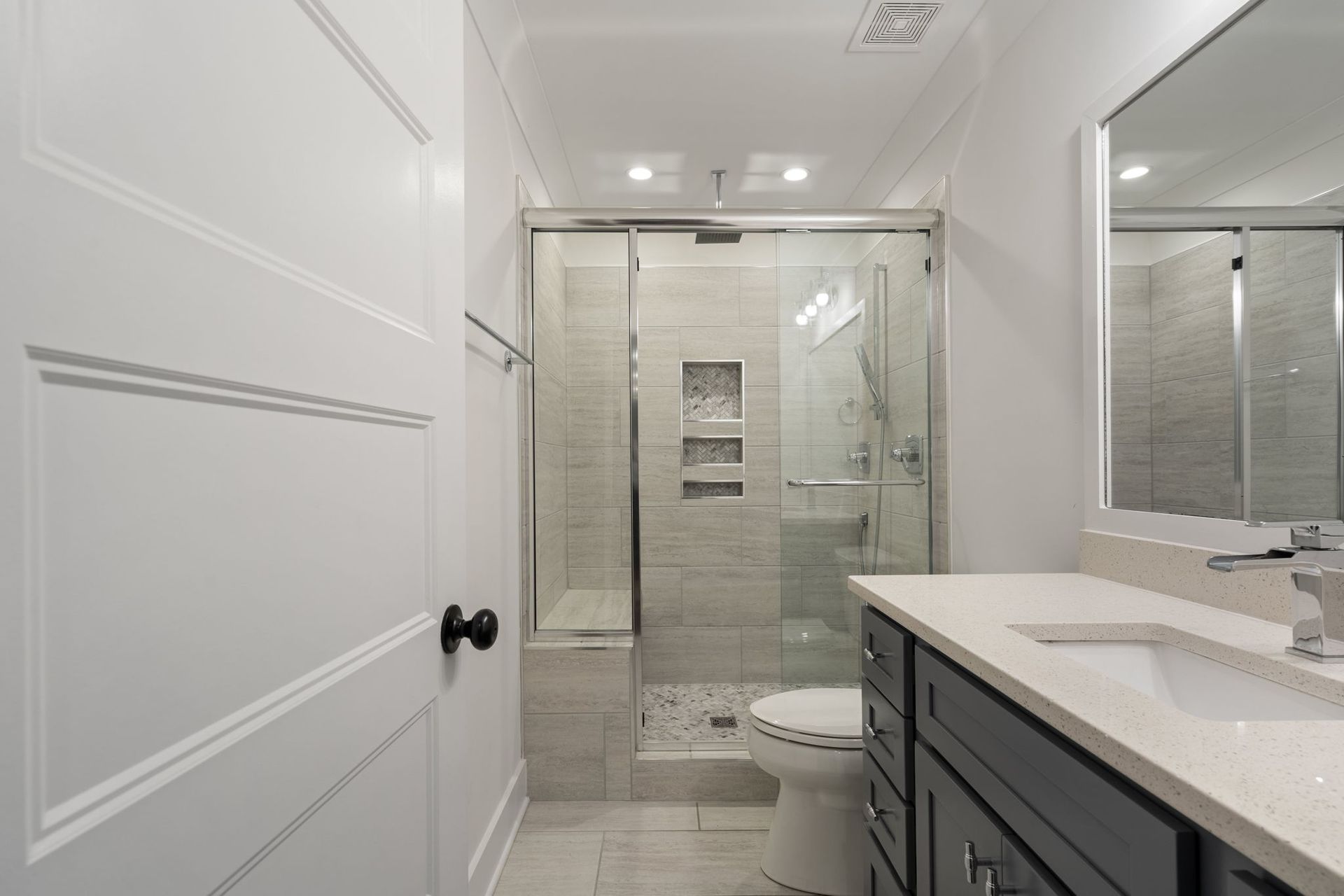 Bright modern bathroom with white walls, glass shower, vanity, and toilet.