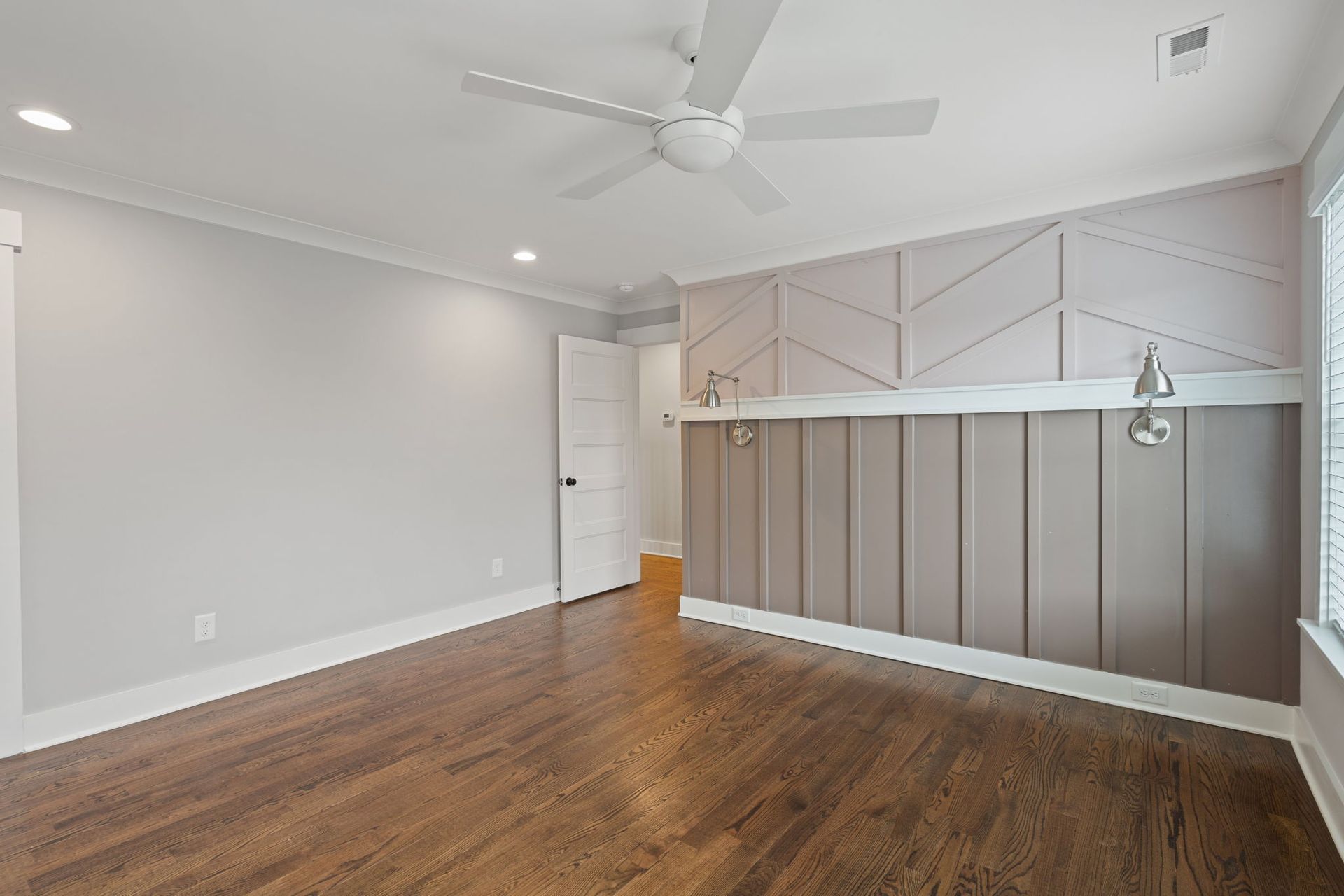 Empty modern living room with hardwood floors, white walls, ceiling fan, and a light gray accent wall.
