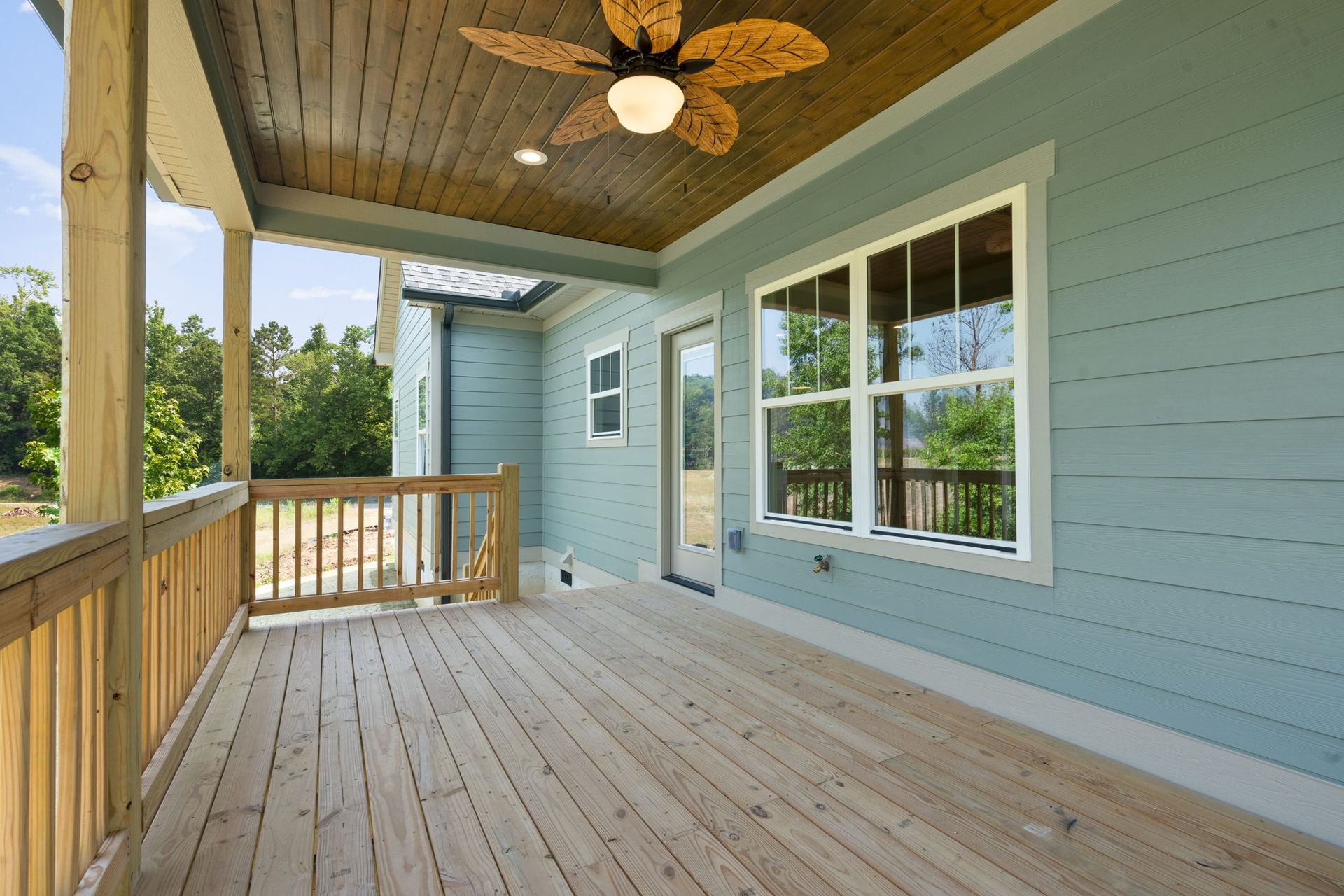 Covered wooden porch with blue siding, white-trimmed windows, and ceiling fan
