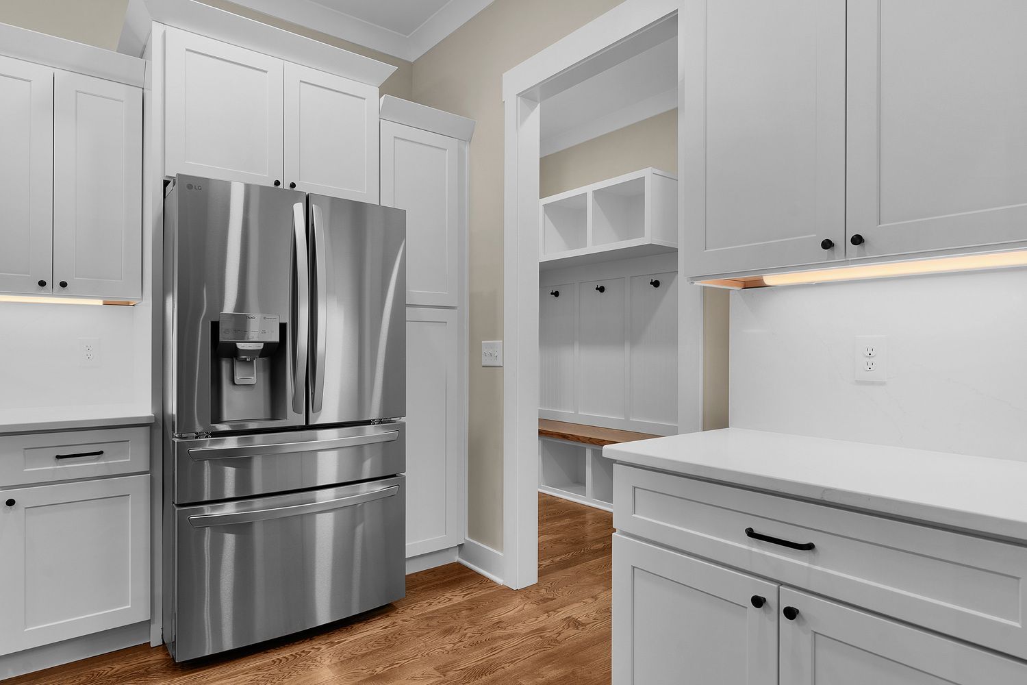 Modern kitchen with stainless steel refrigerator, white cabinets, and wood flooring