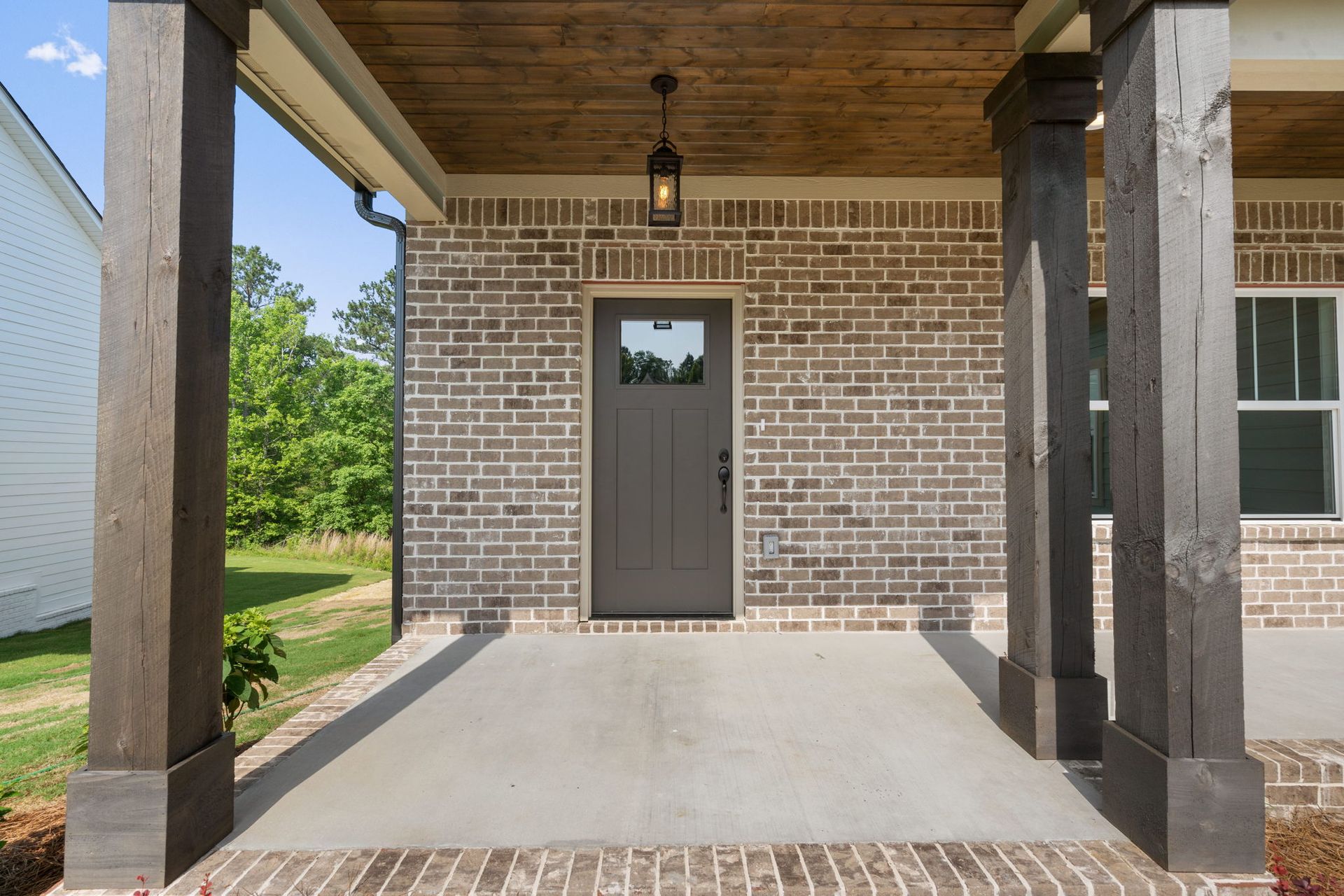 Covered front porch with a gray door, brick wall, and wood posts and ceiling.
