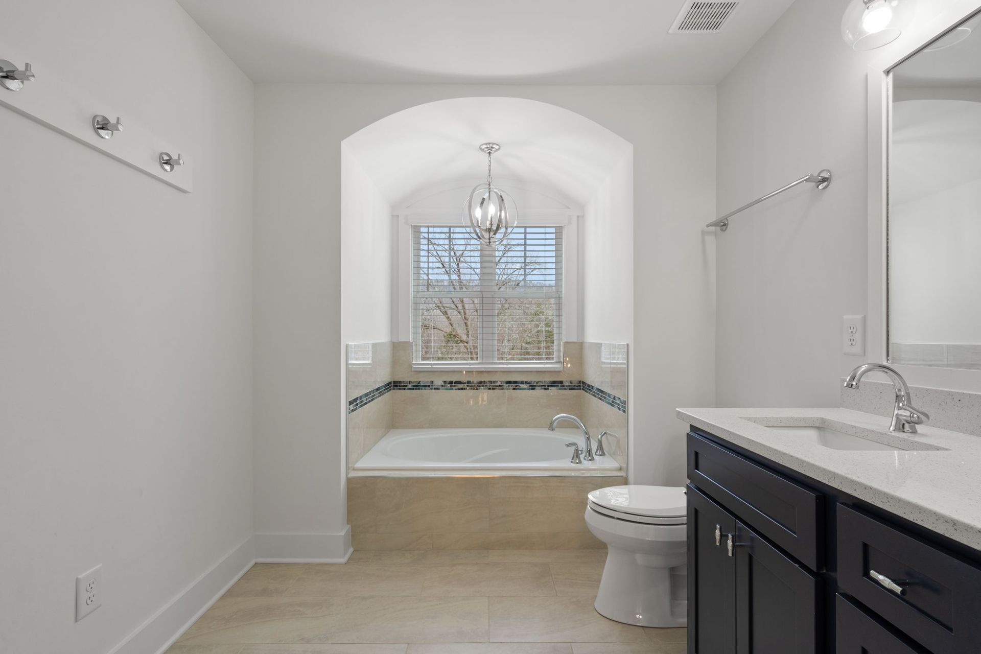 Modern bathroom with double vanity, toilet, and arched soaking tub alcove under a window
