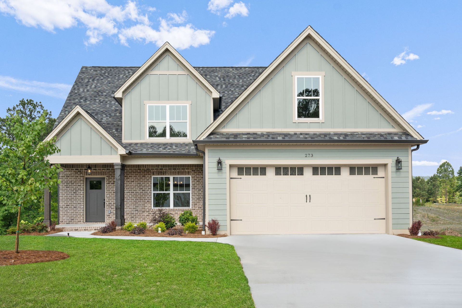 Suburban house with gray siding, stone accents, white garage, and a green lawn under a blue sky