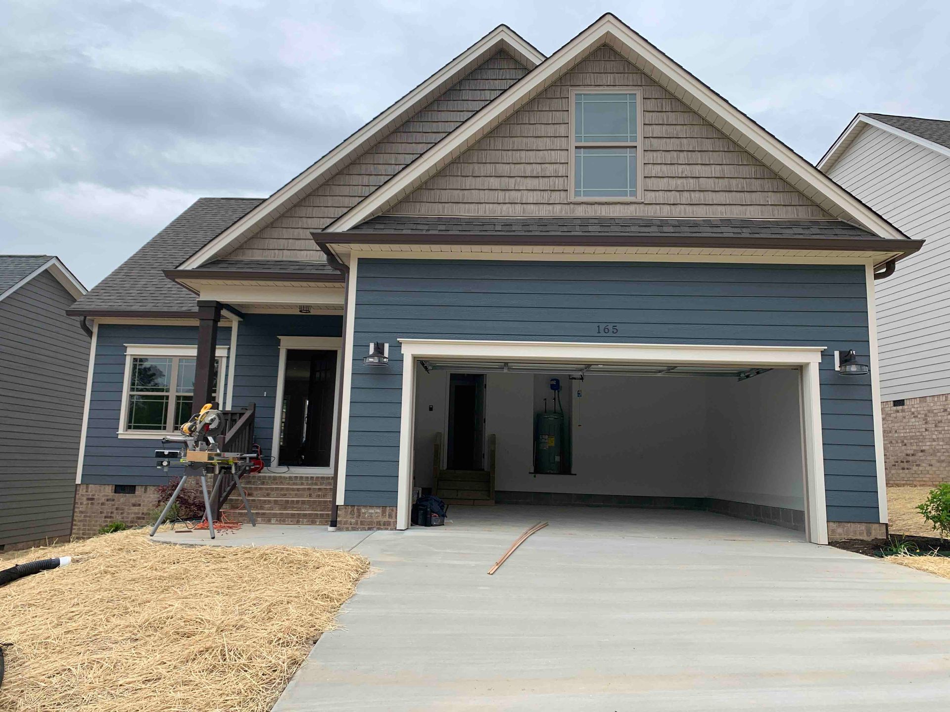 Blue house under construction with open garage and unfinished front yard
