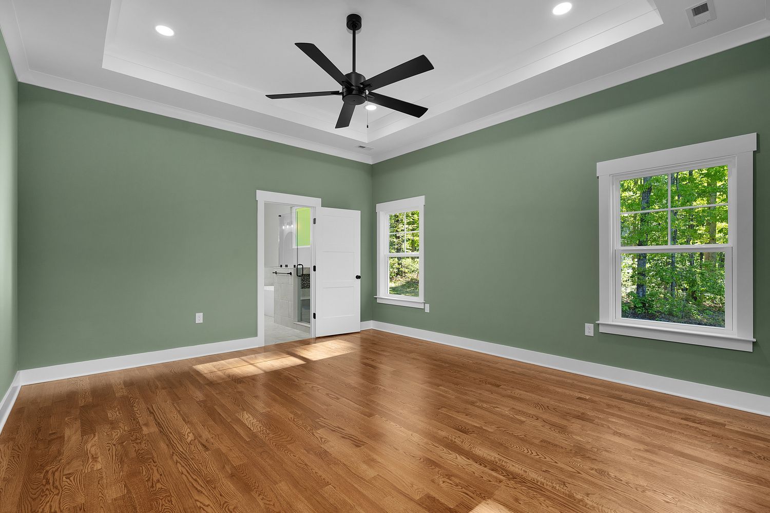 Empty living room with green walls, wood floors, white trim, and ceiling fan under a tray ceiling.