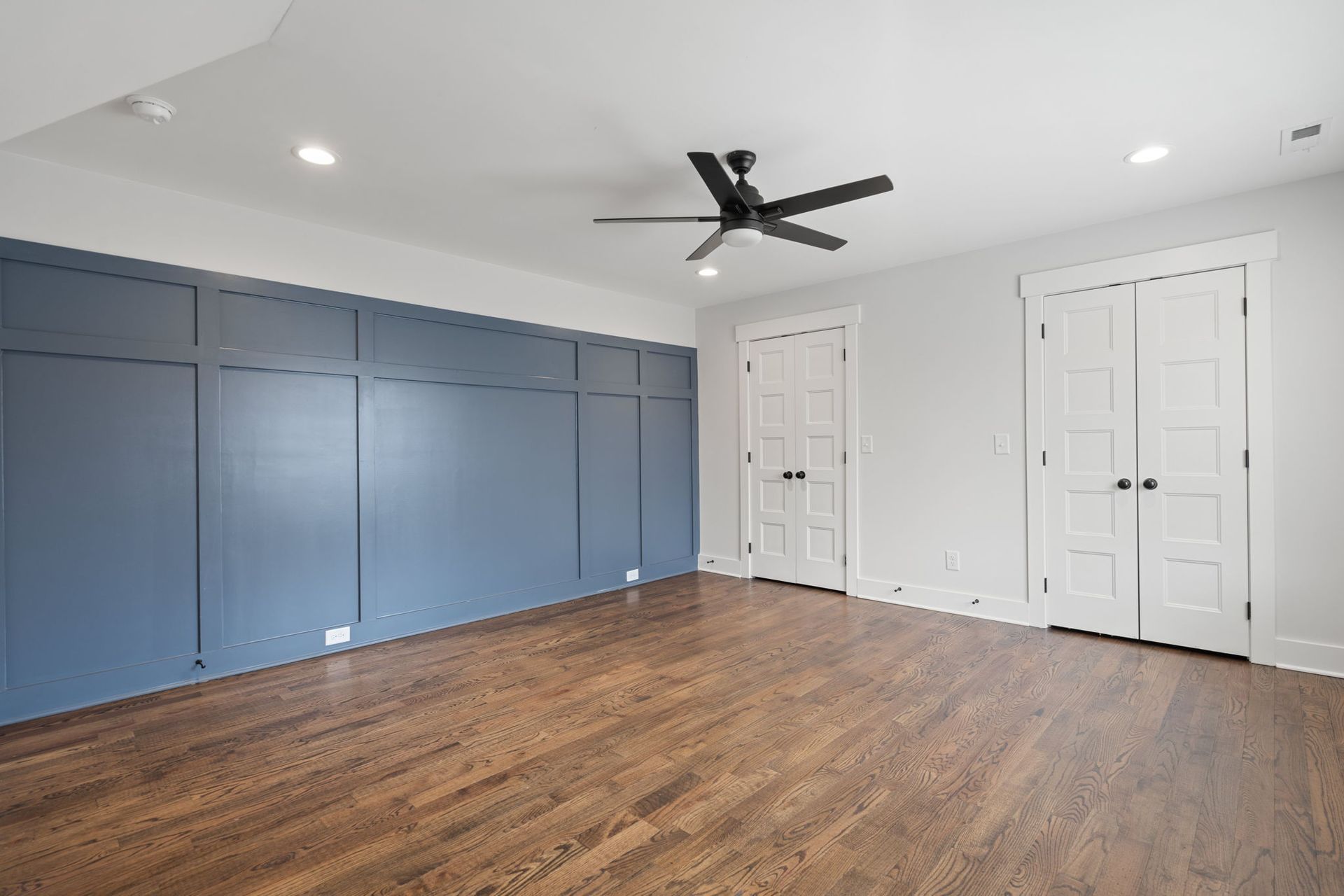 Empty room with blue built-in cabinets, white doors, wood floor, and a black ceiling fan.