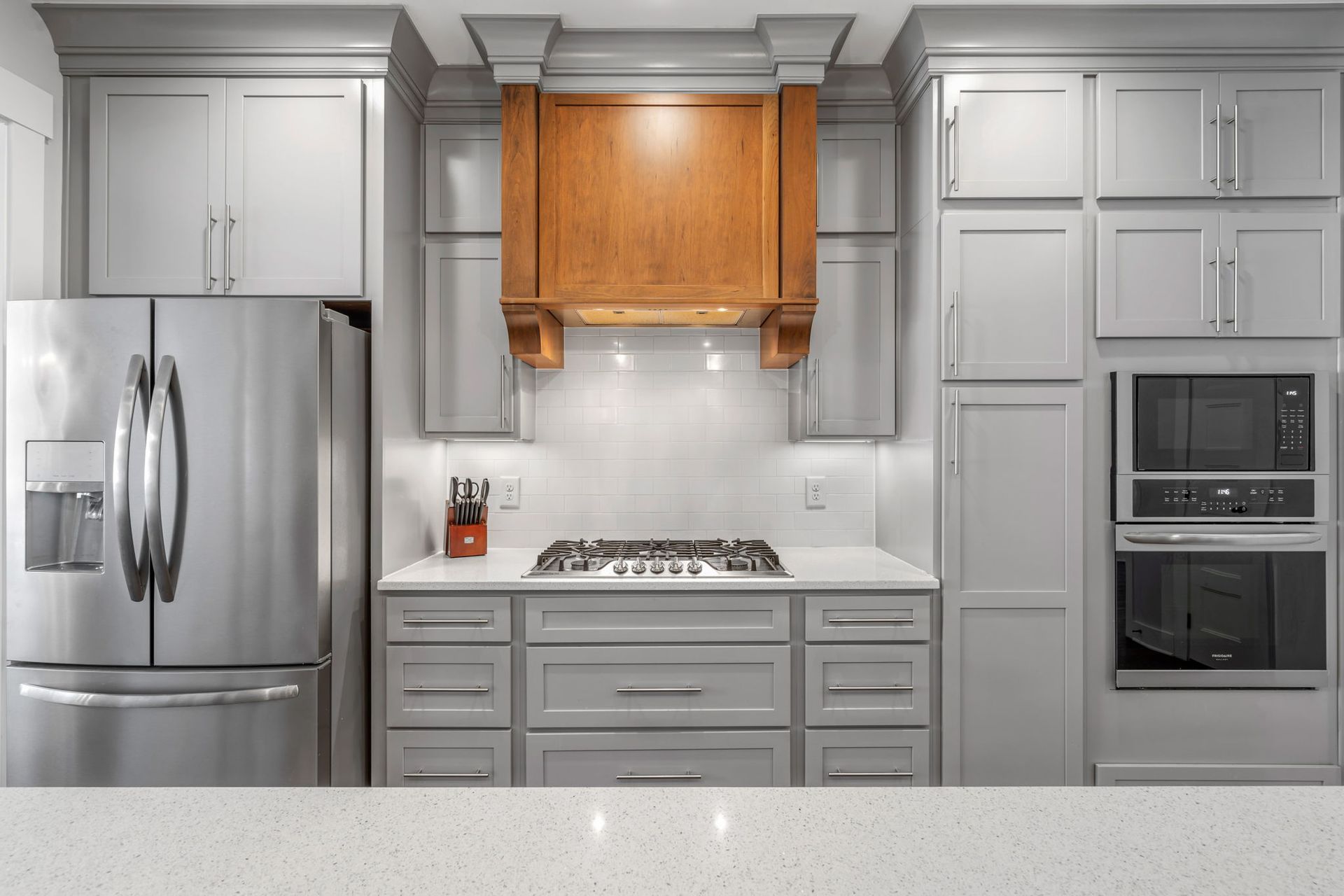 Custom home builder in Chattanooga creates luxury kitchen with gray cabinets, wood range hood, and built-in appliances.