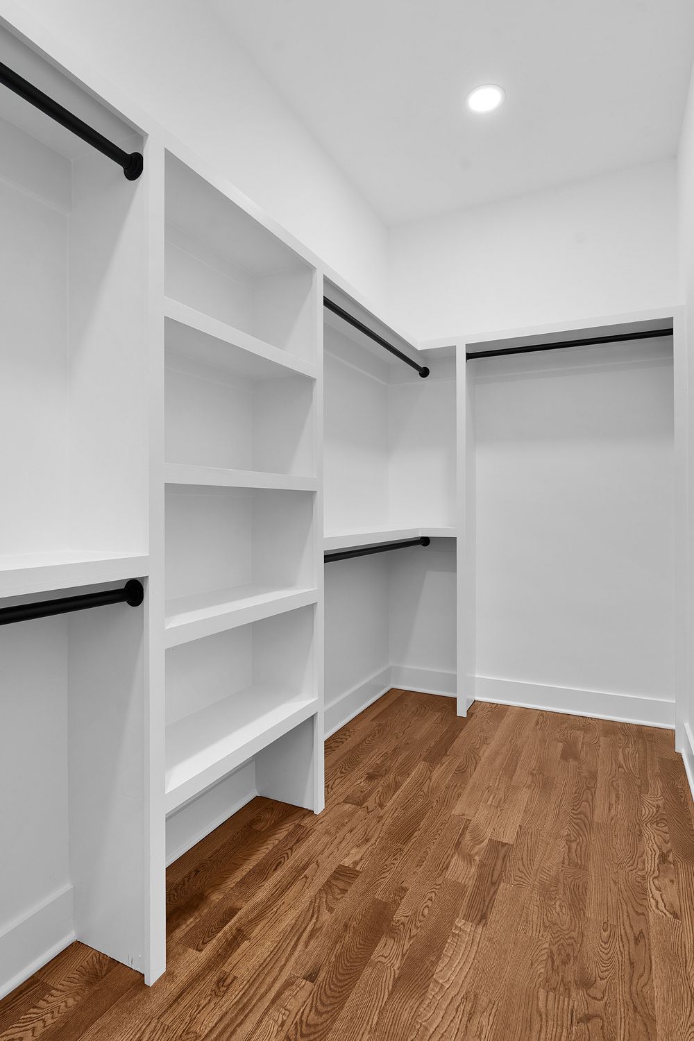 Empty white walk-in closet with shelves, hanging rods, and wood flooring