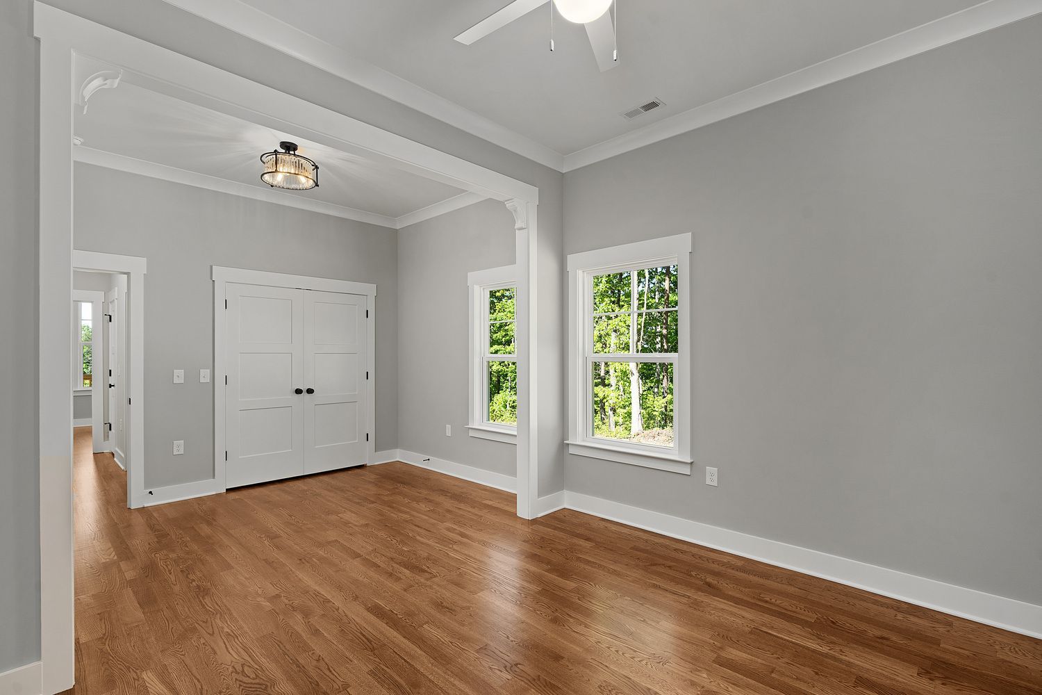 Empty gray living room with hardwood floors, white trim, and bright windows.