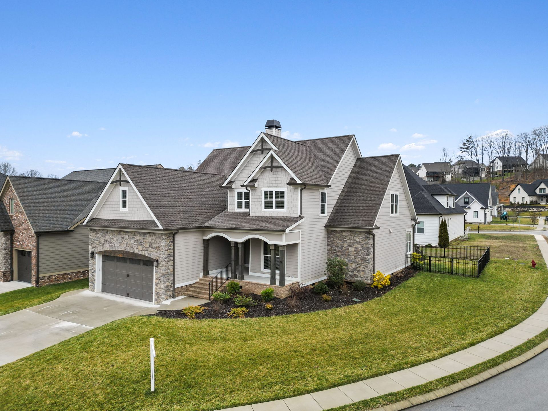 Suburban house with gray stone exterior, front porch, driveway, and manicured lawn on a corner lot