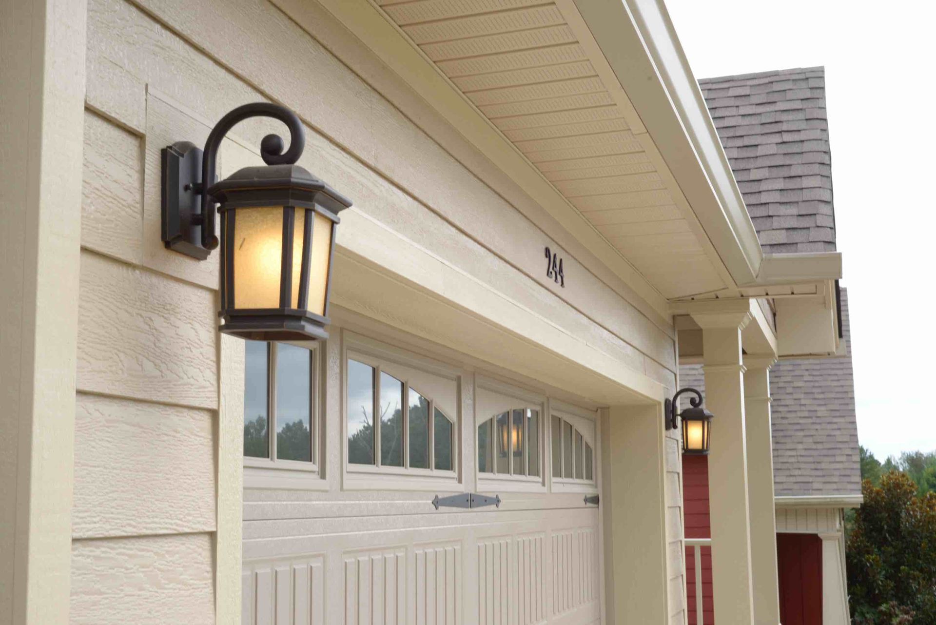 Front porch with black lanterns beside a cream garage door on a house exterior