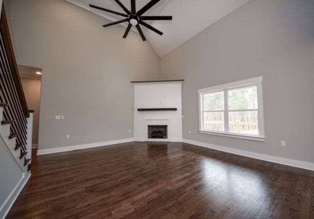 Empty living room with dark hardwood floors, white walls, fireplace, and large window.