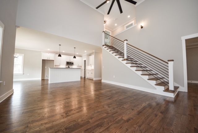 Bright empty modern living room with hardwood floors, white walls, open kitchen, and staircase with metal railing