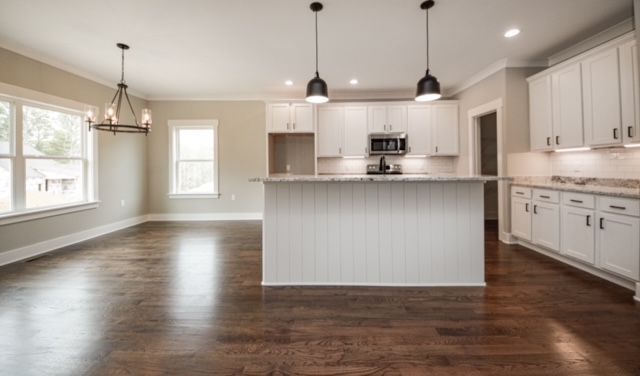 Bright open kitchen with white cabinets, island, dark wood floors, and pendant lights.