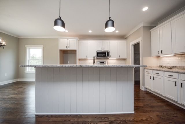 Bright white kitchen with island, pendant lights, dark wood floors, and stainless steel appliances