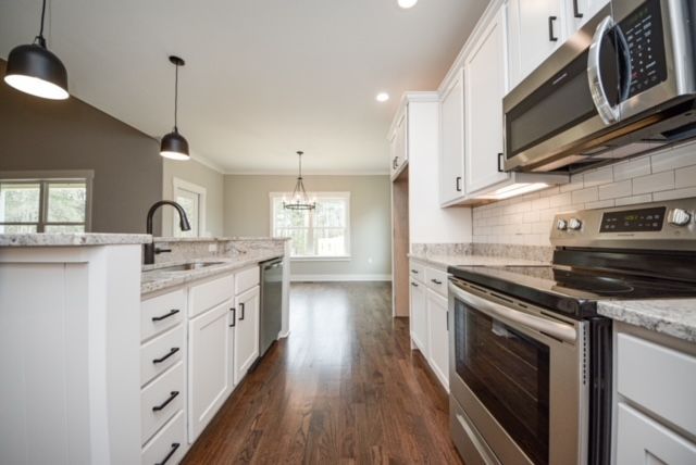 Modern white kitchen with stainless steel appliances, pendant lights, and dark wood flooring