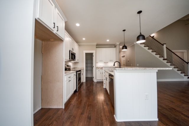 Bright modern kitchen with white cabinets, dark wood floors, island, and staircase in the background