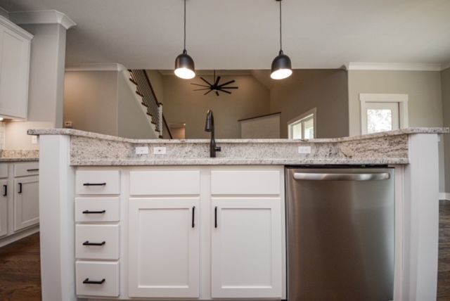 Bright kitchen with white cabinets, granite island, stainless dishwasher, and pendant lights