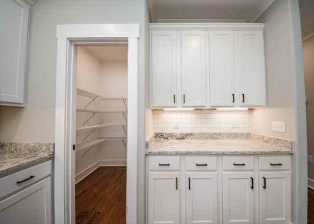 White kitchen cabinets with granite counters and a pantry doorway leading to shelving.