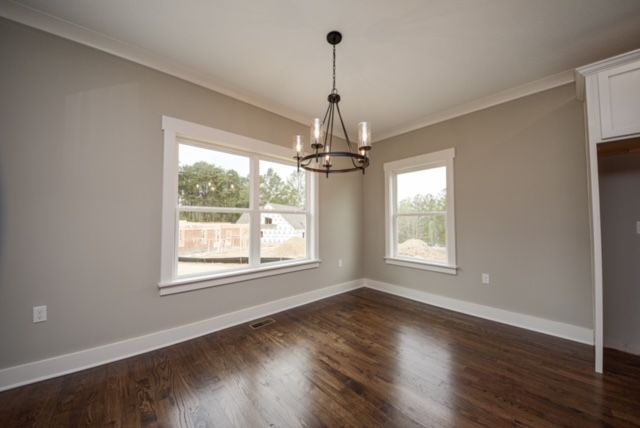 Empty dining room with dark wood floors, gray walls, large windows, and a black chandelier.